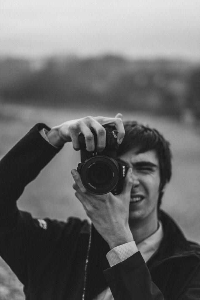 Black and white image of a man taking a photo with a DSLR camera outdoors.